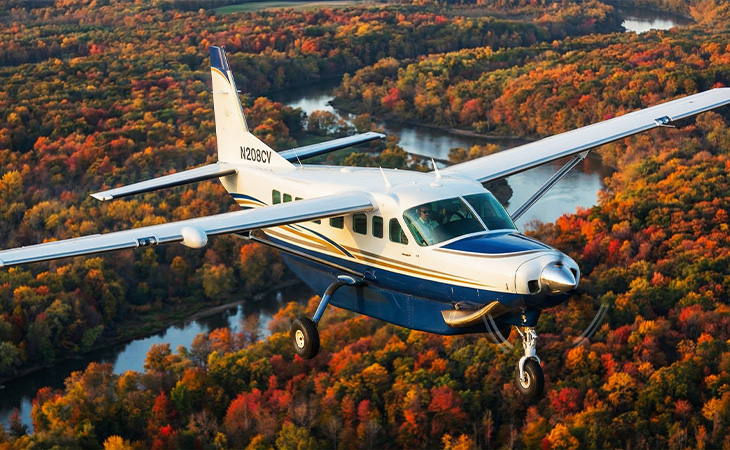 Cessna 208 Caravan turboprop aircraft cruising above colorful fall landscape