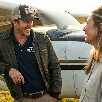Pilot and aviation enthusiast apparel including trucker hat, polo, and jacket displayed near a small aircraft, highlighting personalized aviation apparel brand