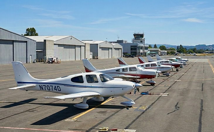 Private aircraft lineup on tarmac at regional airport with hangars and control tower in background.
